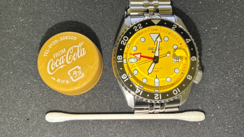 A size comparison photo of the SKX Style GMT placed next to a plastic bottle cap and a cotton swab.